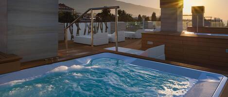Un jacuzzi con vistas a montañas y al atardecer.