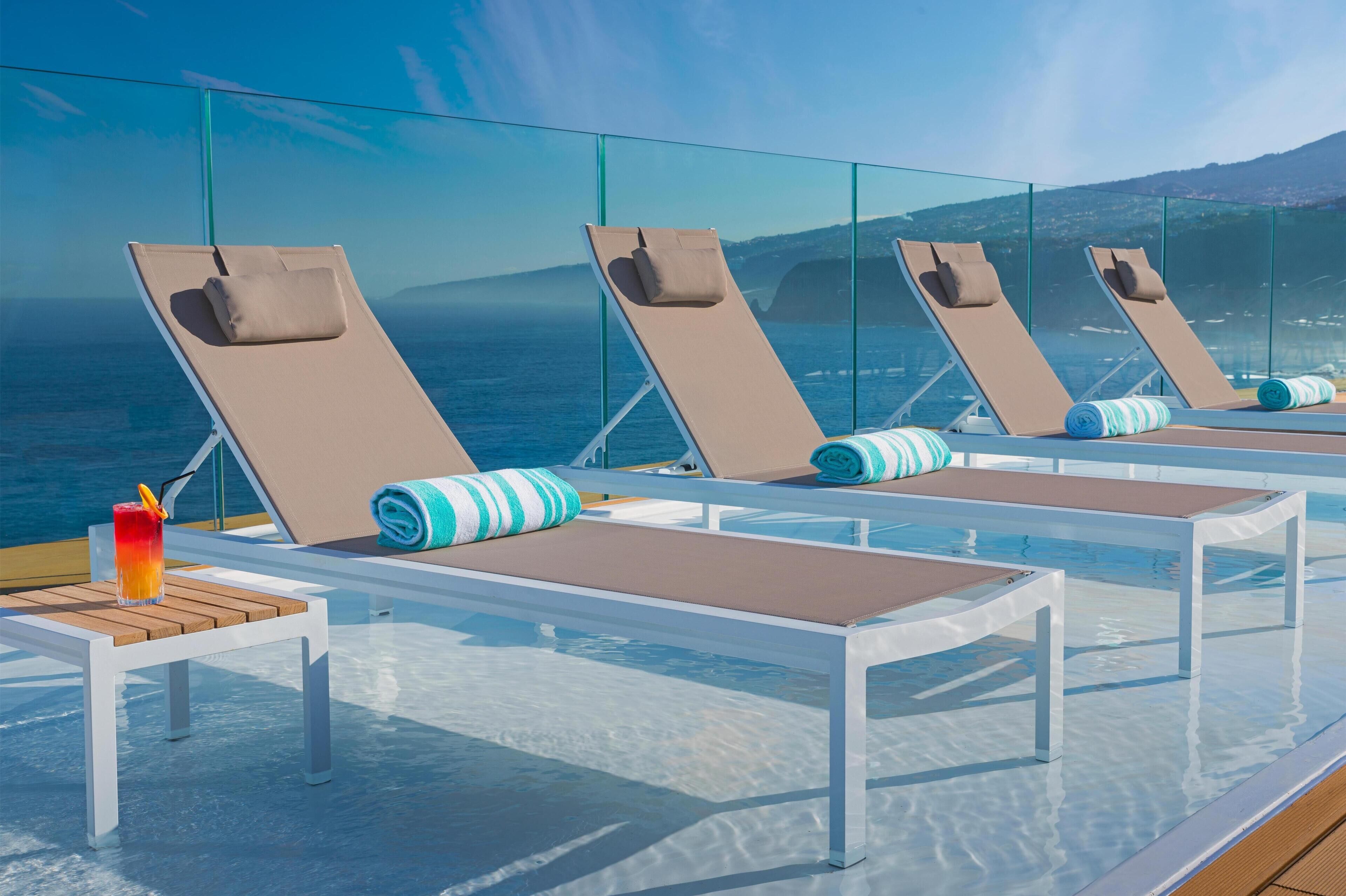 A poolside area with lounge chairs and a table, overlooking the sea.