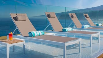 A poolside area with lounge chairs and a table, overlooking the sea.