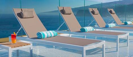 A poolside area with lounge chairs and a table, overlooking the sea.