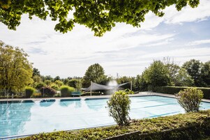 Piscina com área cercada por rede, rodeada por vegetação e árvores.