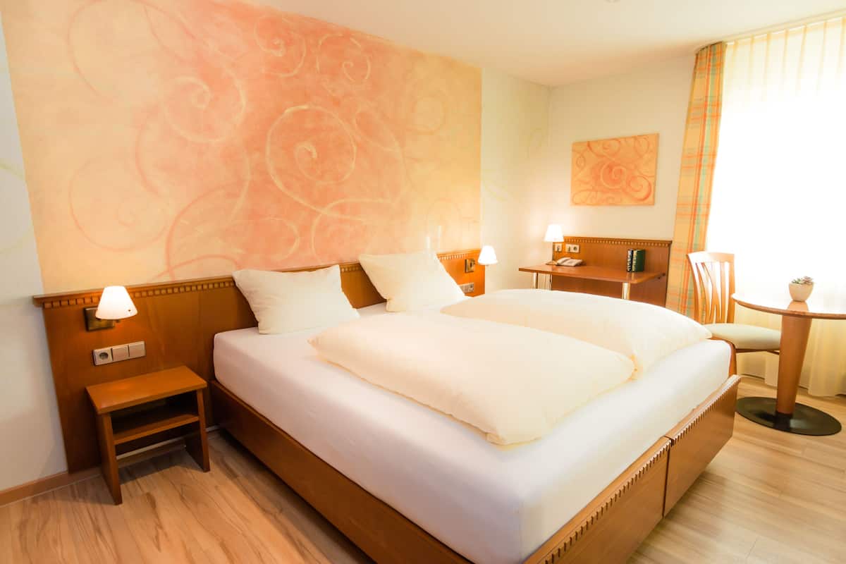 A hotel room with a large bed, bedside lamps, a small table, and a chair.