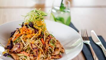 A plate of stir-fried noodles with vegetables and chicken, accompanied by a glass of iced tea.
