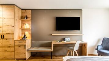 A modern bedroom with a wooden desk, a flat-screen TV, a grey armchair, and a bed.