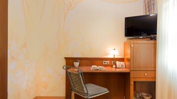 Habitación de hotel con escritorio de madera, una silla, televisor sobre el escritorio y un mueble bajo con cajones.