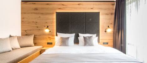 A modern bedroom with a wooden headboard, a bed with white linens, a wooden bench, and two bedside lamps.