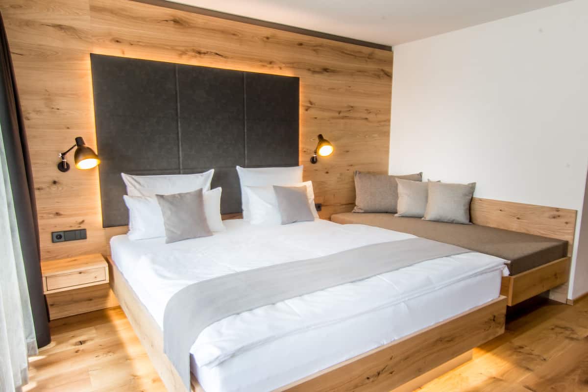 A modern bedroom with a large bed, a smaller sofa bed, wooden paneling, and wall-mounted reading lights.