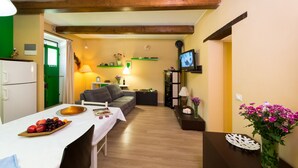 A cozy living room with a dining table set with fruit, a sofa, and a TV on a shelf. - Casa Lina (Castiglion Fiorentino)