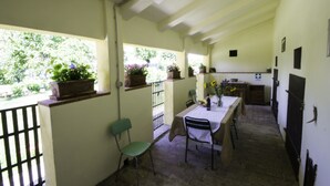 A narrow corridor with a table and chairs, potted plants, and a view of greenery outside. - Casa Lina (Castiglion Fiorentino)