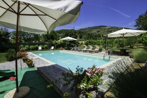 Una piscina con sillas de descanso y sombrillas, rodeada de vegetación y un paisaje montañoso.