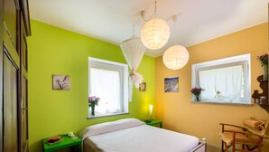 A bedroom with a bed, bedside tables, a chair, and two windows with curtains. - Casa Lina (Castiglion Fiorentino)
