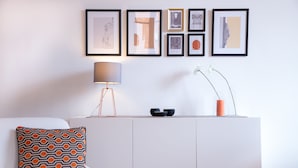 A modern living room with a white sofa, a patterned throw pillow, a lamp, and a wall-mounted shelf with decorative items. - Casa Frangiò - Naples Historical Centre (Naples)