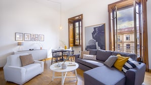 A modern living room with a white sofa, a grey sofa, and a round coffee table. There are framed pictures on the wall and a window with a view of buildings. - Casa Frangiò - Naples Historical Centre (Naples)