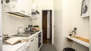 A narrow kitchen with white tiles, a stove, sink, and a small countertop with a kettle and cups. - Casa Frangiò - Naples Historical Centre (Naples)