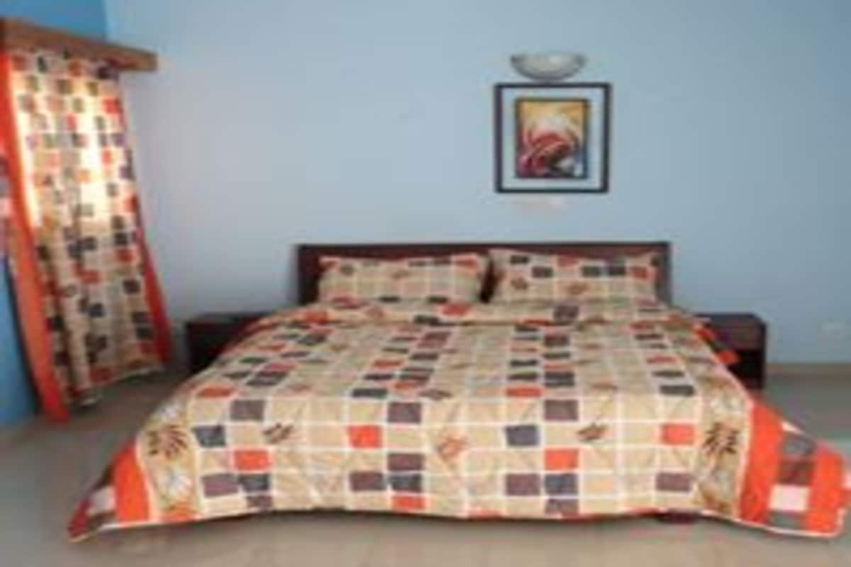 A bedroom with a bed, a nightstand, a wall-mounted shelf, and a window with curtains.