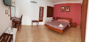 Un dormitorio con cama, escritorio, silla, espejo y ventana.