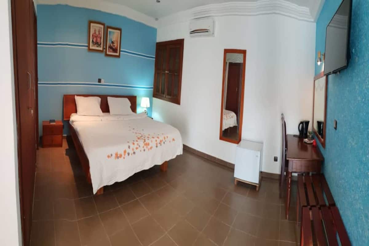 A bedroom with a bed, bedside table, dresser, mirror, and a small table with a lamp.