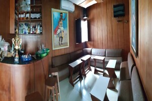 Una zona de bar con paneles de madera, una barra con un trofeo y un área de asientos con mesas y sillas.