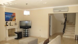 A living room with a flat-screen TV, a fireplace, a sofa, and a staircase. - Anemon Solovilla (Fethiye)