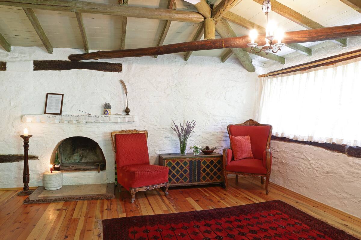 A rustic room with a fireplace, two red armchairs, wooden flooring, and a chandelier.