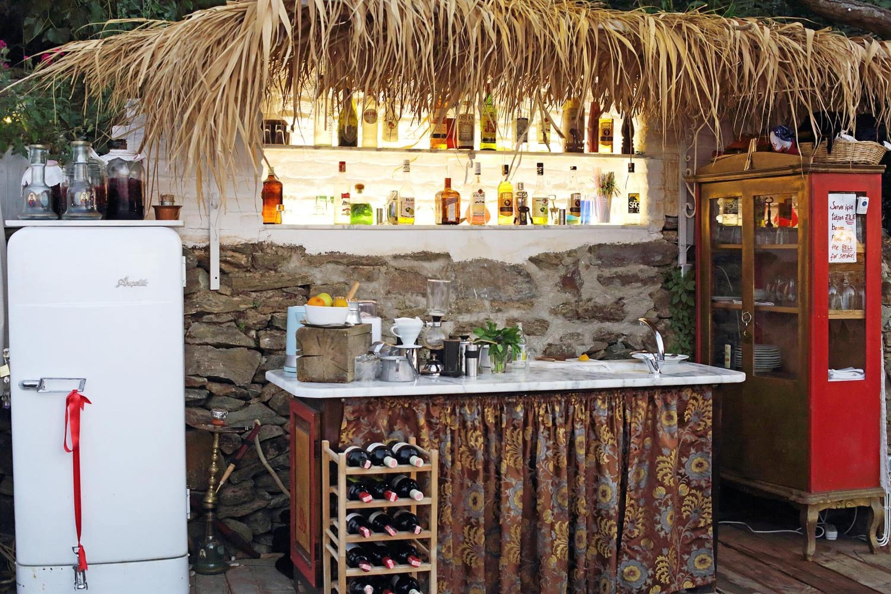 A rustic bar area with a thatched roof, a refrigerator, a wine rack, and a cabinet with a glass door.