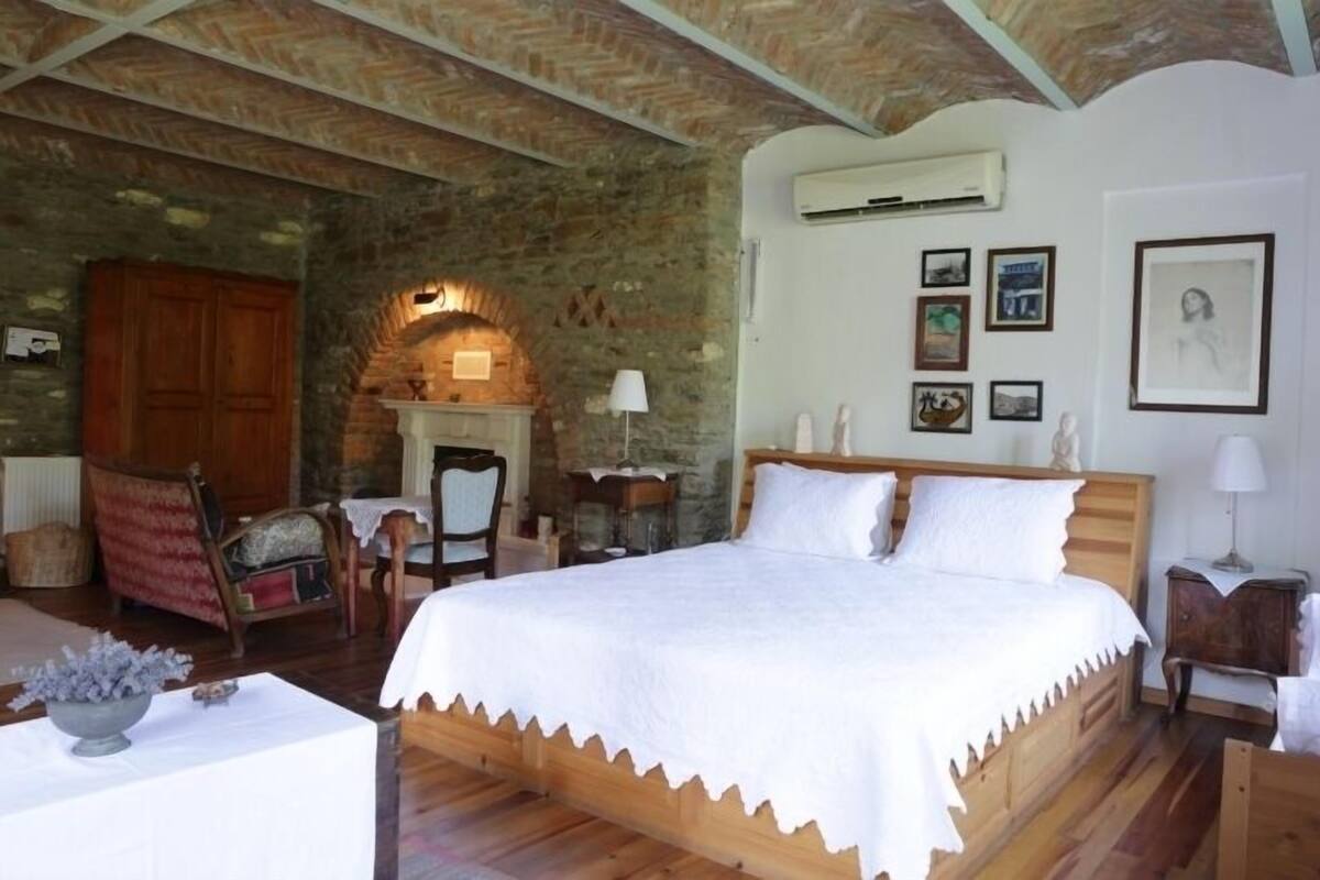 A bedroom with a wooden bed, a stone fireplace, and a rustic stone wall.