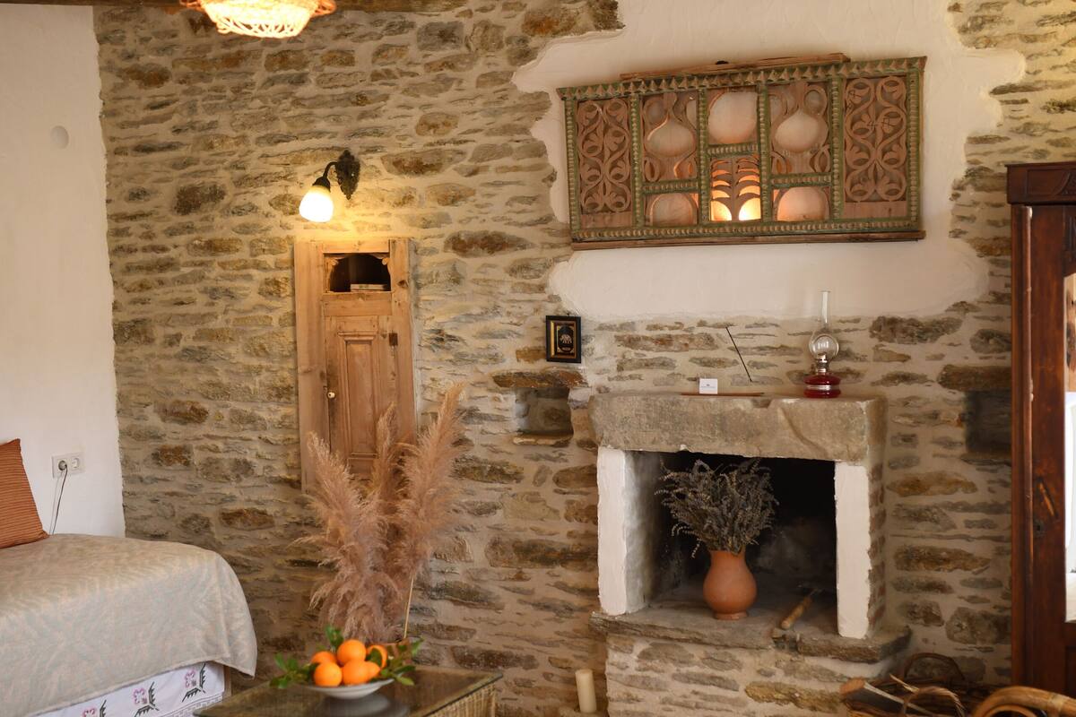 A rustic room with a stone wall, a fireplace, a bed, a wicker table, and a hanging light fixture.