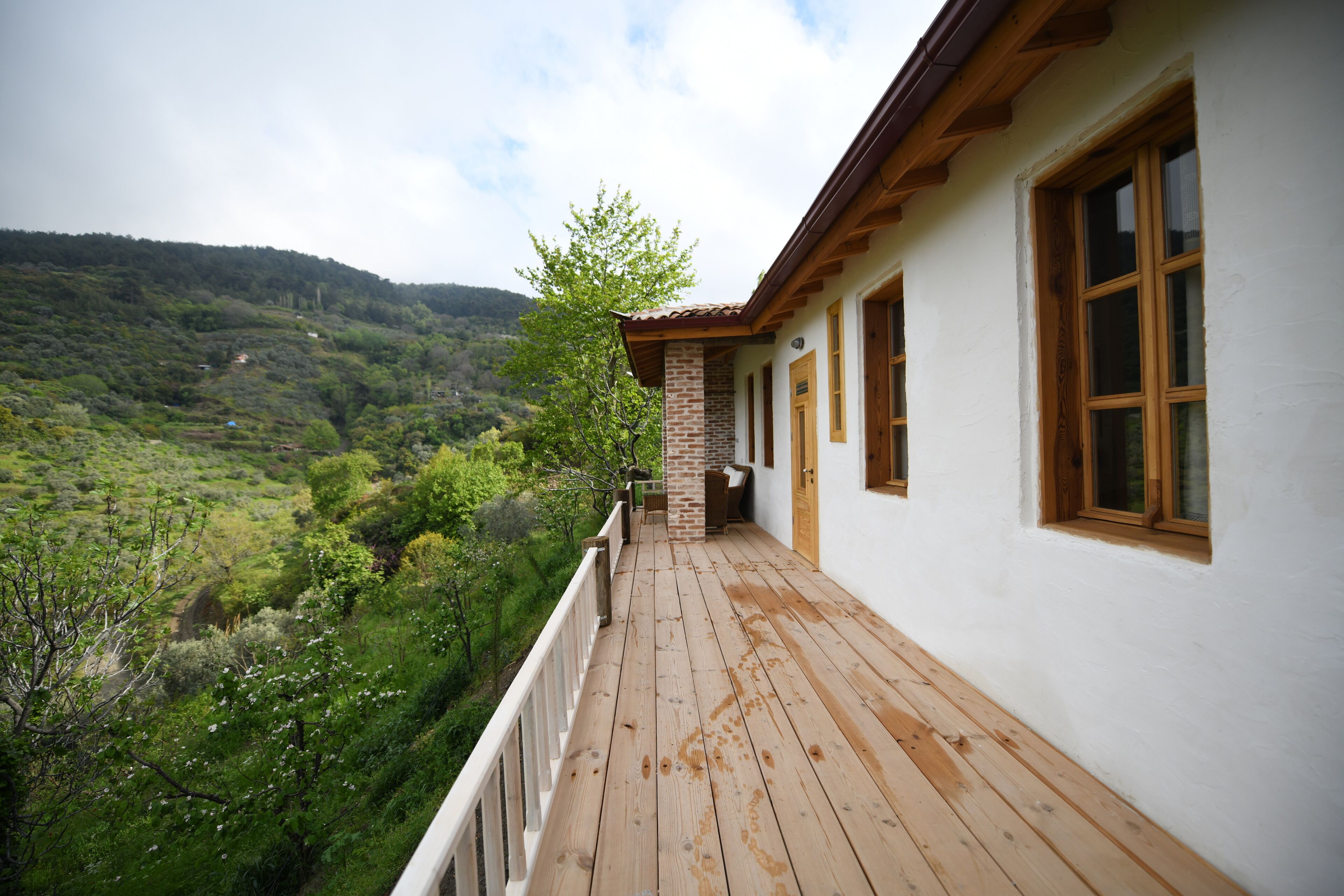 A wooden deck with a white building, a brick column, and a view of a green valley.