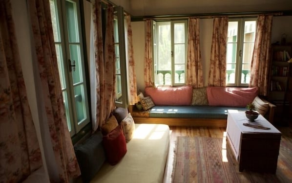 A cozy room with a built-in bench, a small table with a bowl, and a bookshelf. - Nisanyan Hotel (Selçuk)