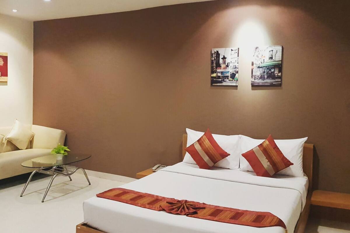 A hotel room with a bed, a sofa, a small table, and two wall-mounted pictures.