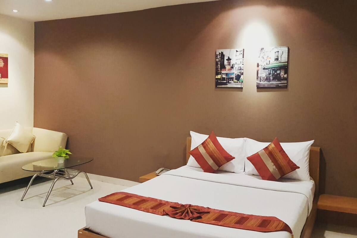 A hotel room with a bed, a sofa, a small table, and two wall art pieces.