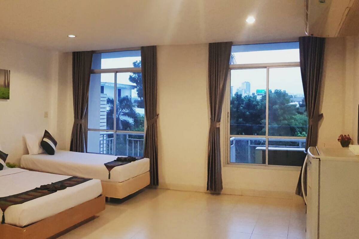A hotel room with two beds, a small table, a TV, and large windows with curtains.