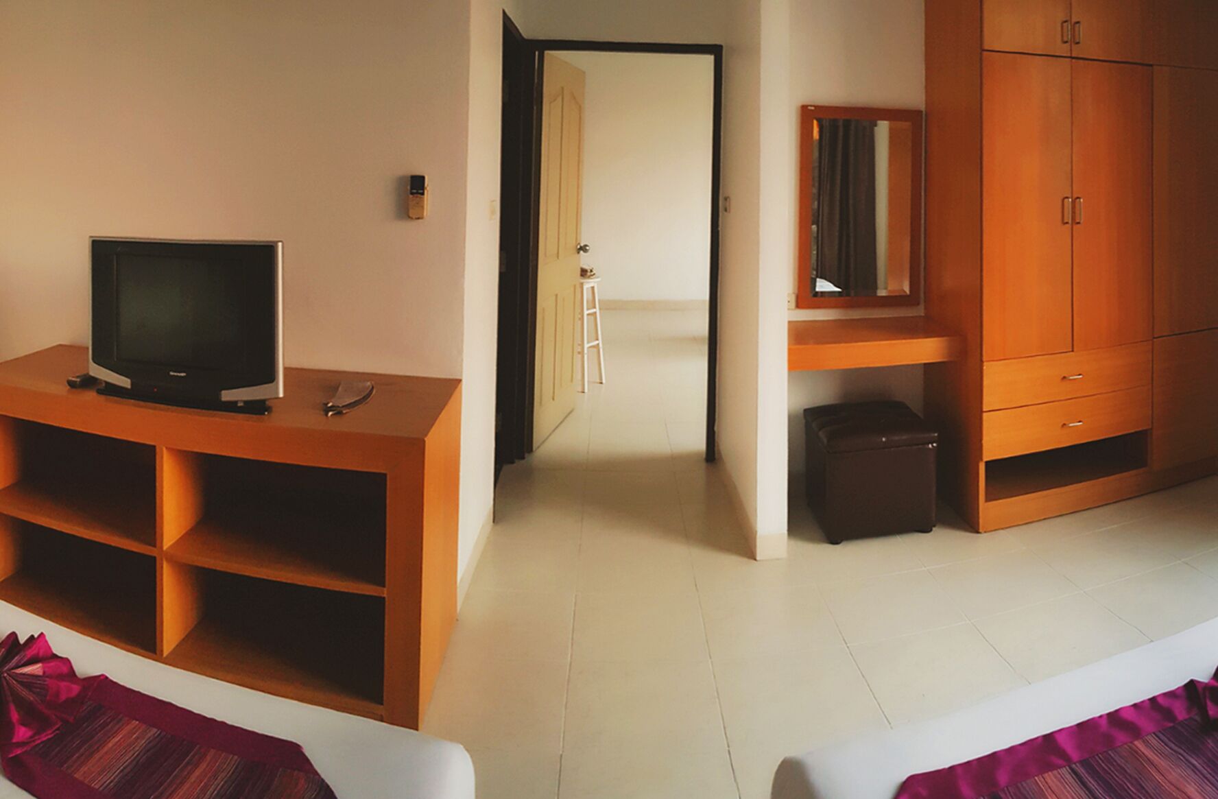 Quarto com televisão sobre suporte de madeira, guarda-roupa e espelho.