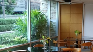 A modern meeting room with glass tables and wooden chairs, large windows with a view of greenery, and a whiteboard on the wall. - Sena house Paholyothin30 (Bangkok)