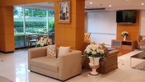 A modern hotel lobby with a sofa, a brown armchair, a glass coffee table, and a TV mounted on the wall. - Sena house Paholyothin30 (Bangkok)