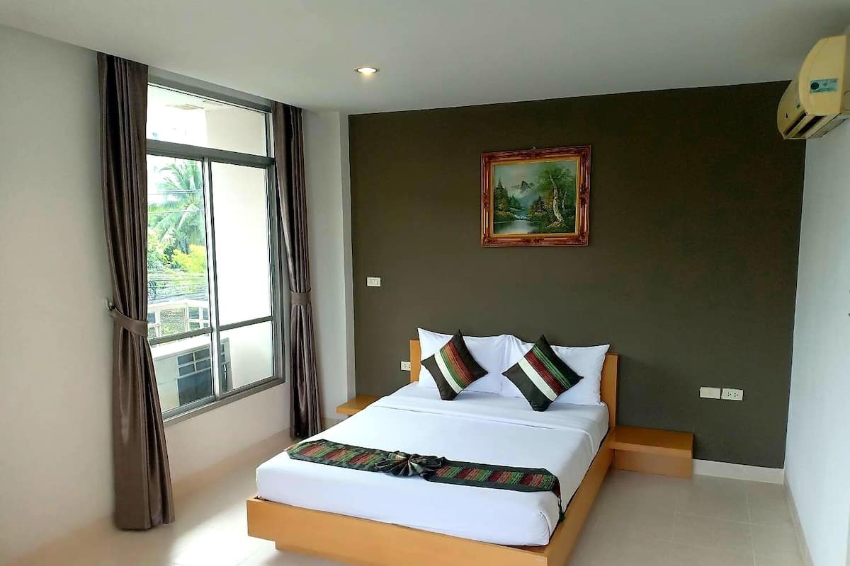 A bedroom with a bed, a window with curtains, a painting on the wall, and a ceiling light.