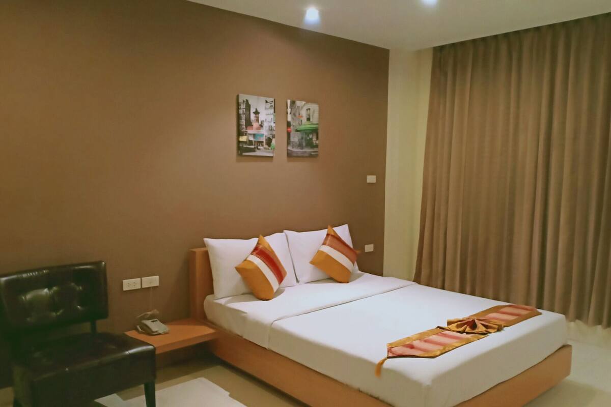 A hotel room with a large bed, a nightstand, a chair, and two wall-mounted artworks.