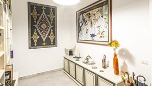 Une pièce avec un mur blanc, une armoire blanche, un vase de fleurs et deux œuvres d’art encadrées.
