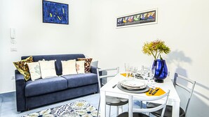 Un salon moderne avec un canapé bleu, une table à manger blanche et des œuvres d’art accrochées aux murs.