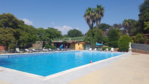 A rectangular swimming pool with clear blue water, surrounded by lounge chairs and a small building with a red roof. - Camping Aurelia Club (Rome)