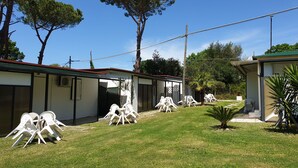 A row of single-story buildings with outdoor seating areas, surrounded by trees and a clear sky. - Camping Aurelia Club (Rome)