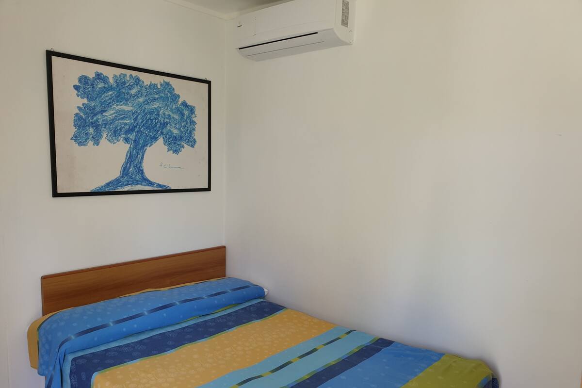 Ein Einzelbett mit Holz-Kopfteil, einer farbenfrohen, gestreiften Bettdecke und einem gerahmten Bild eines Baumes an der Wand.
