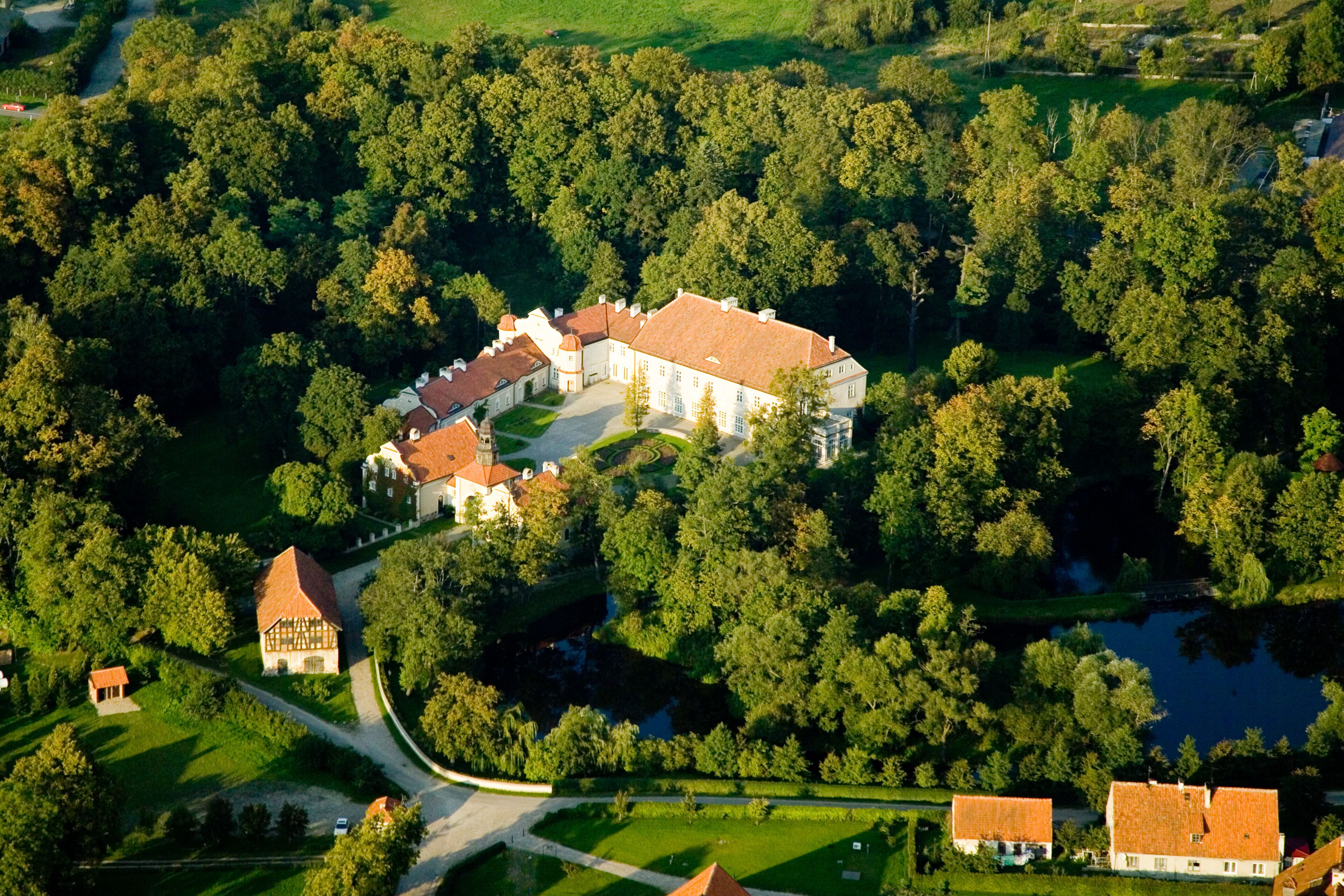 An aerial view of a large estate with multiple buildings, surrounded by dense forests and a lake.