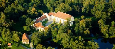 An aerial view of a large estate with multiple buildings, surrounded by dense forests and a lake.