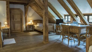 Una habitación rústica con vigas de madera a la vista, un escritorio de madera con sillas, una cama y un televisor.