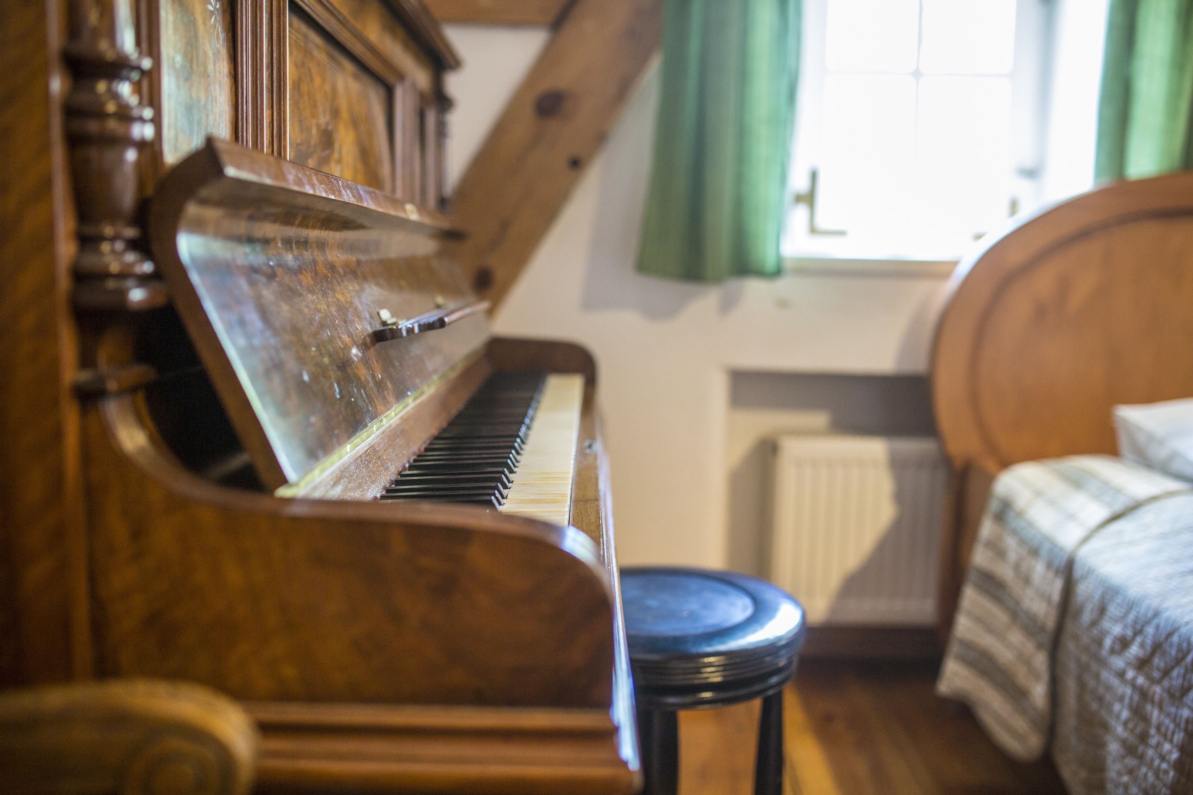 A wooden piano in a room with a bed and a radiator.