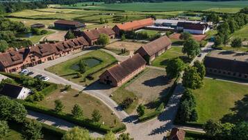 An aerial view of a rural estate with multiple buildings, including barns and a large house, surrounded by green fields and a small pond.