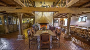 Un comedor rústico con una gran mesa de madera y sillas, una chimenea y vigas de madera en el techo.