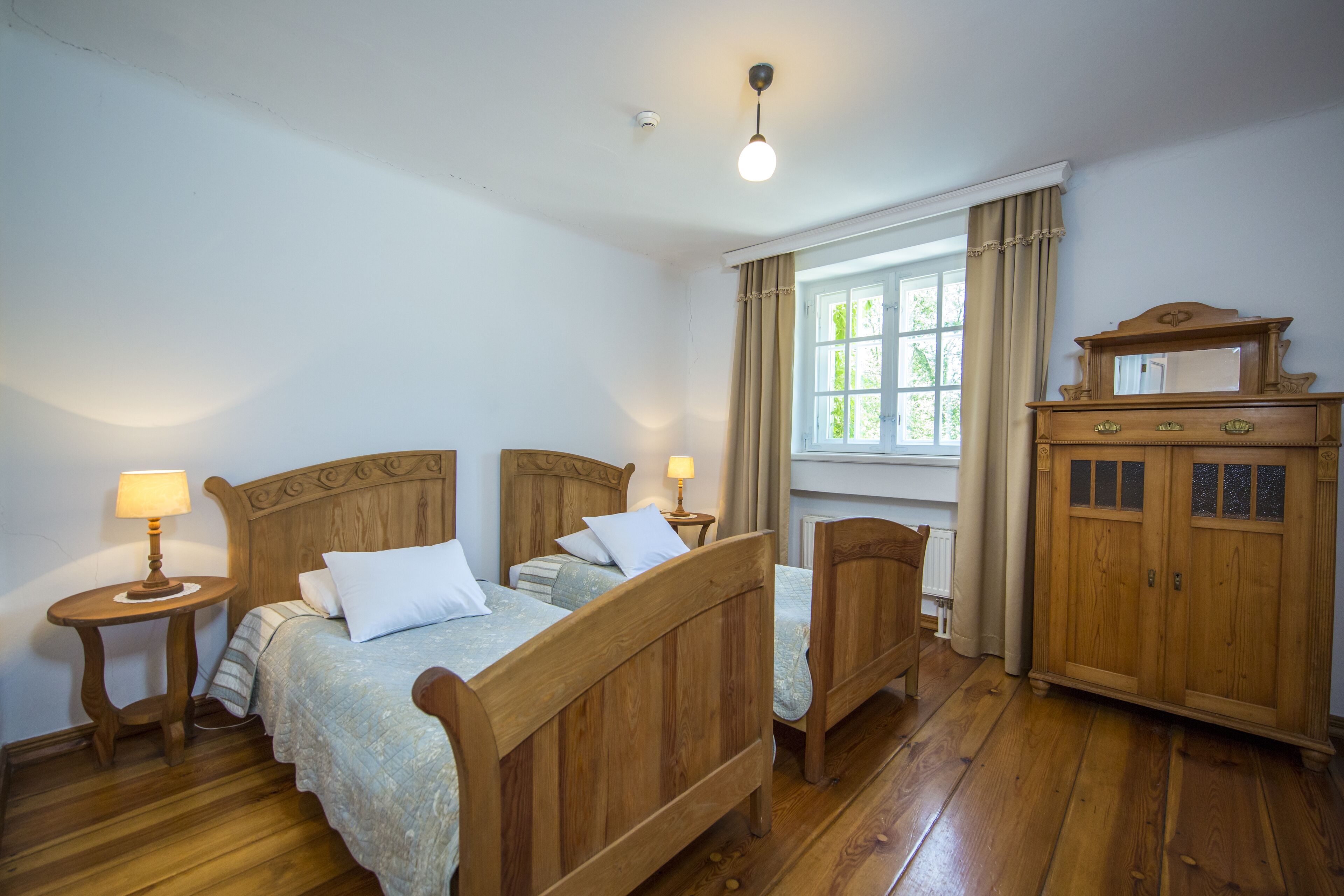 Quarto com cama de madeira, mesas de cabeceira, penteadeira e janela com cortinas.