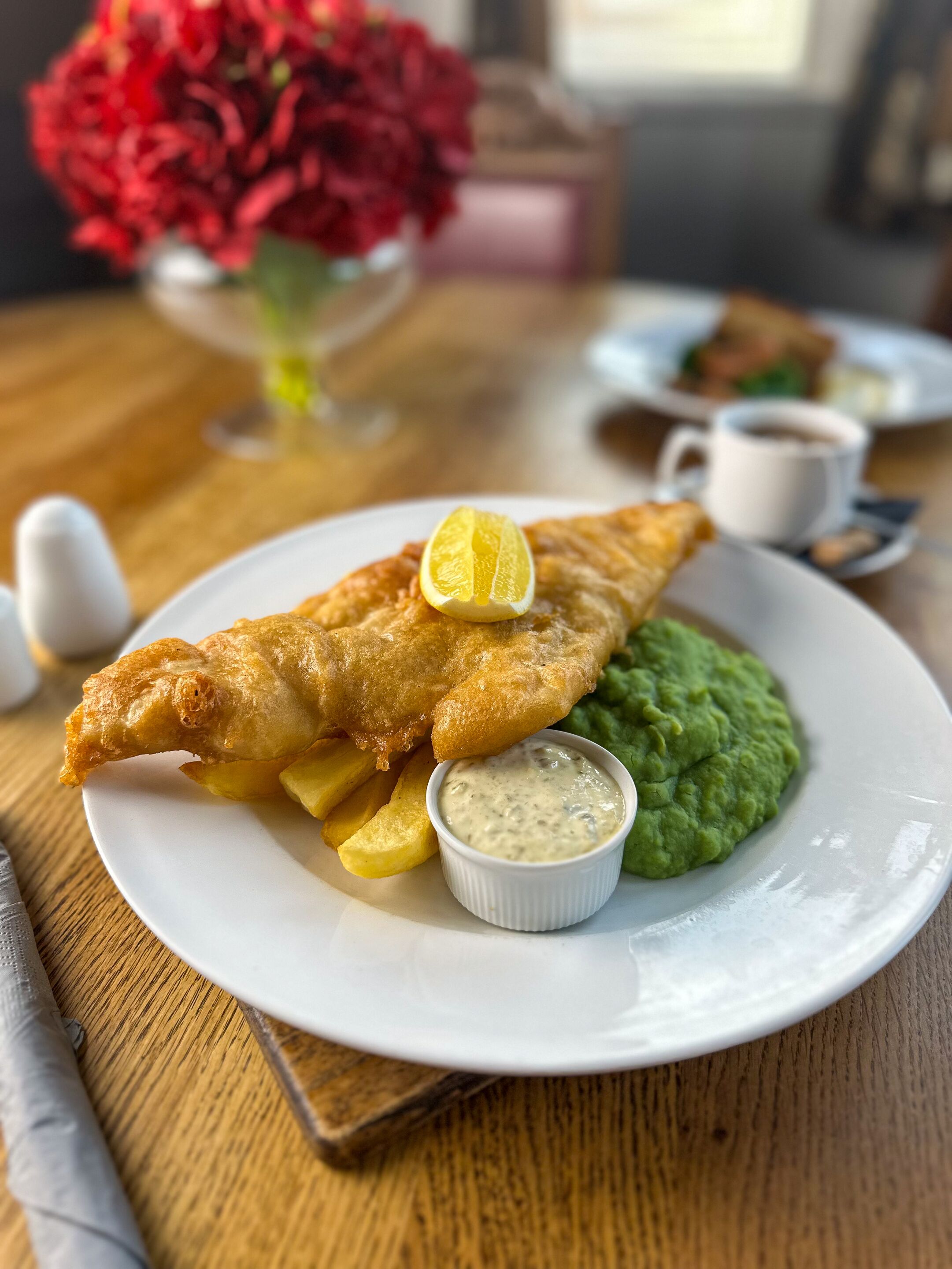 A plate of fish and chips with lemon wedges and a side of mushy peas.